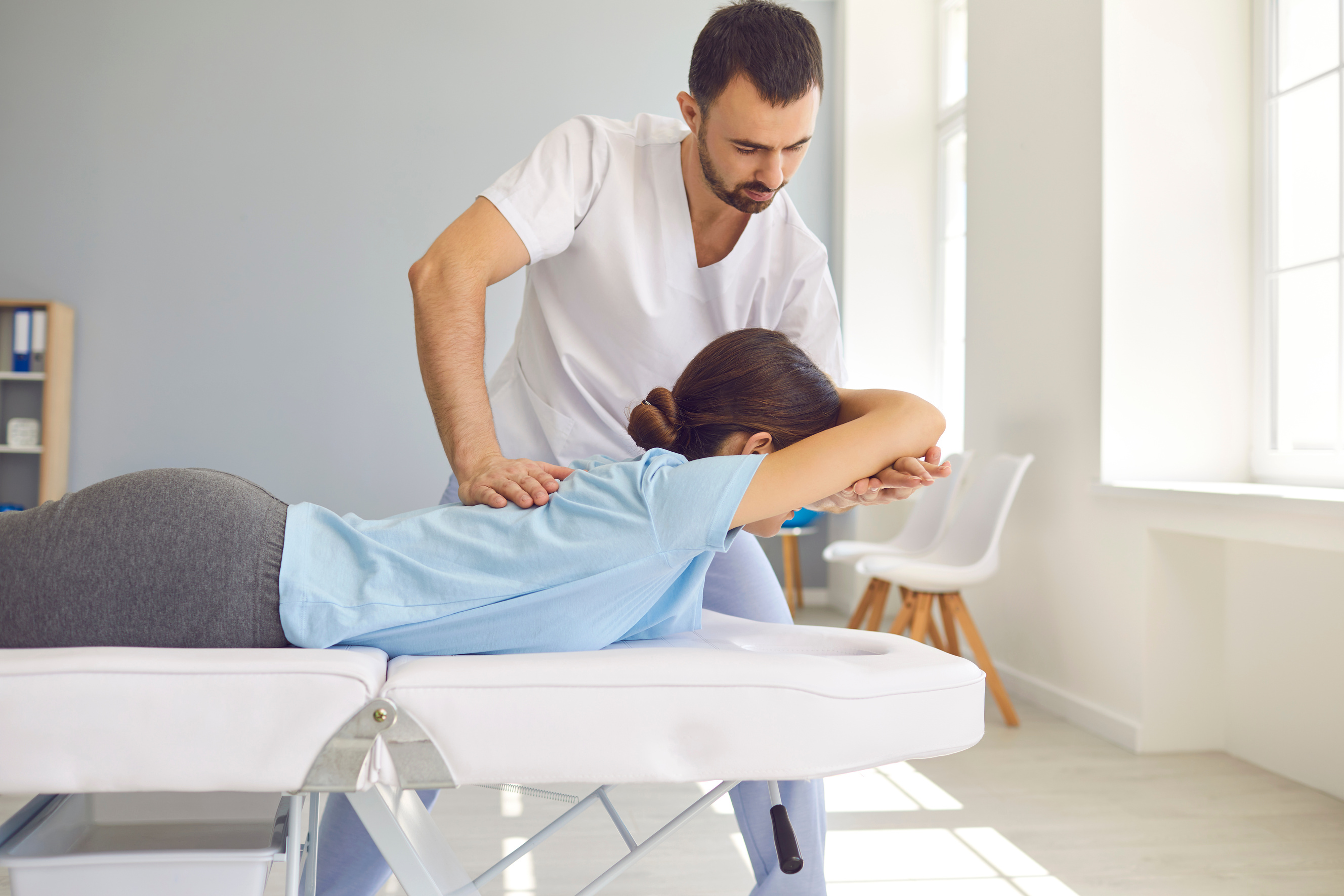 Professional Doctor Doing Chiropractic Back Adjustment to Female Patient in Modern Health Center